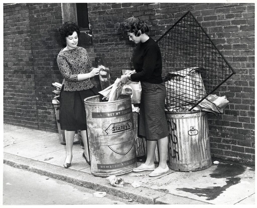 Two women placing rubbish into a Boston trash can in a historical City of Boston photograph.