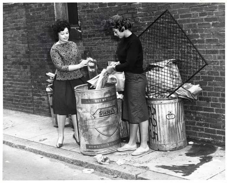 Two women placing rubbish into a Boston trash can in a historical City of Boston photograph.